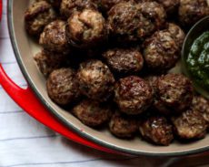 baked meatballs in a red dish with pesto on the side
